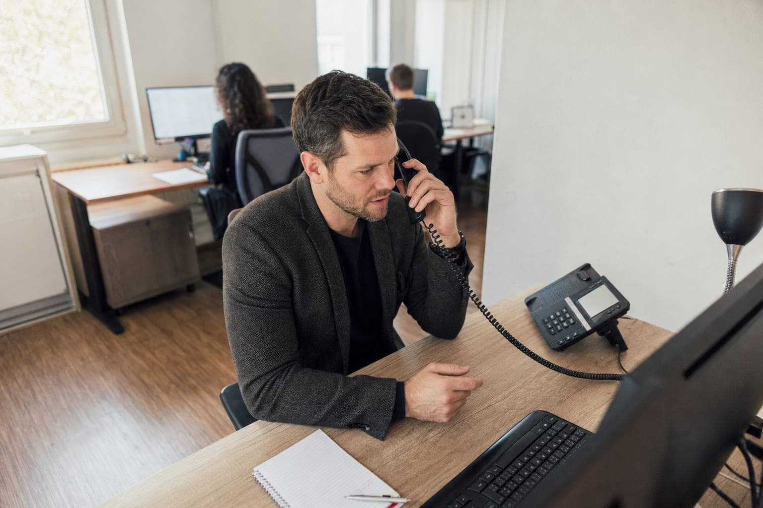 Recruiter im Büro am Telefon, daneben Notizblock und Tischapparat